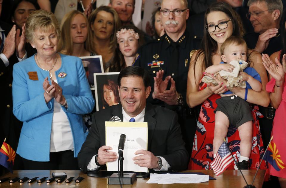 Arizona Republican Gov. Doug Ducey, middle, smiles after signing into law a bill regarding distracted driving as he is joined by legislators, like bill sponsor Kate Brophy McGee, left, R-Phoenix, members of law enforcement and family members of victims of distracted drivers, during a ceremony at the Arizona Capitol Monday, April 22, 2019, in Phoenix. Arizona becomes the 48th state to ban texting and the 18th to ban any hand-held phone use while driving. Officers can begin issuing warnings immediately and can write tickets in 2021. (AP Photo/Ross D. Franklin)