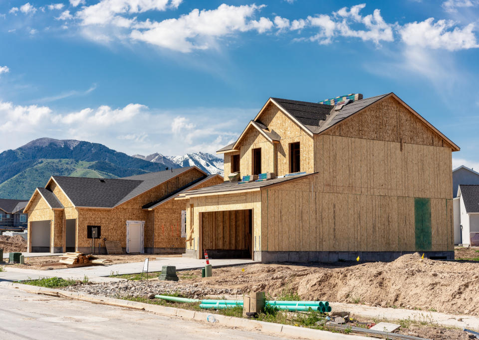 Unfinished houses under construction with exposed wooden frames and roofing work in progress, and no windows on one side