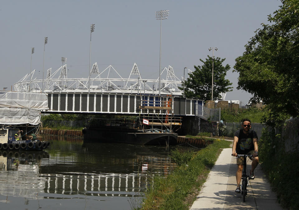 A cyclist passes by the Olympic Stadium on a canal side cycle path in London, Thursday, May 24, 2012. There are many cycle paths across London that can be used to travel the capital. Like a runner or a swimmer, you would need to be physically fit. Like a goalie or a boxer, you should be prepared for close calls. But if you are coming to London's Summer Olympics _ and you have what it takes _ using a bicycle could be a great option in a city bracing for gridlock. (AP Photo/Kirsty Wigglesworth)