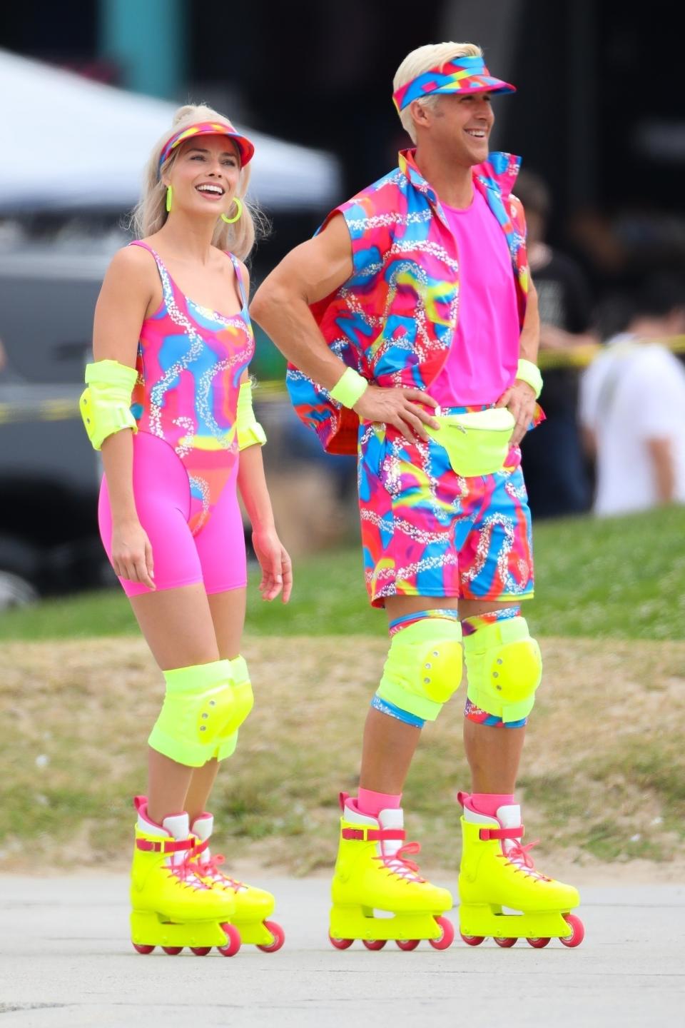 Margot Robbie and Ryan Gosling share a laugh as they film a rollerblading scene for 'Barbie' in Venice Beach in very bright and colorful neon attire.