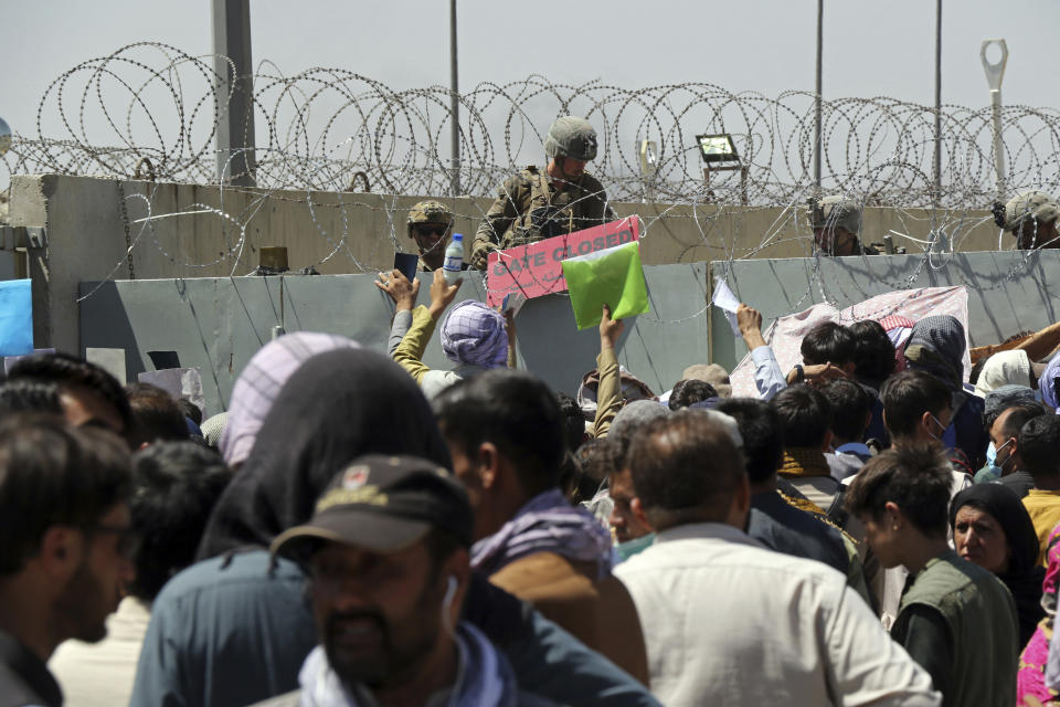 FILE - In this Aug. 26, 2021, file photo, a U.S. soldier holds a sign indicating a gate is closed as hundreds of people gather near an evacuation control checkpoint on the perimeter of the Hamid Karzai International Airport, in Kabul, Afghanistan. Many U.S. citizens and green card holders are still in the Afghan capital despite official promises that every American who wants to leave Afghanistan would be taken out. (AP Photo/Wali Sabawoon, File)