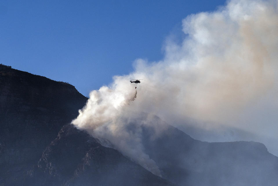 A South African military helicopter drops his water load on the top of Table Mountain in Cape Town, South Africa, Tuesday April 20, 2021. Fire crews worked for a third day to extinguish a wildfire on the slopes of Cape Town's Table Mountain on Tuesday as the city came to terms with the damage caused by what officials have described as one of the area's worst blazes in years. (AP Photo/Jerome Delay)