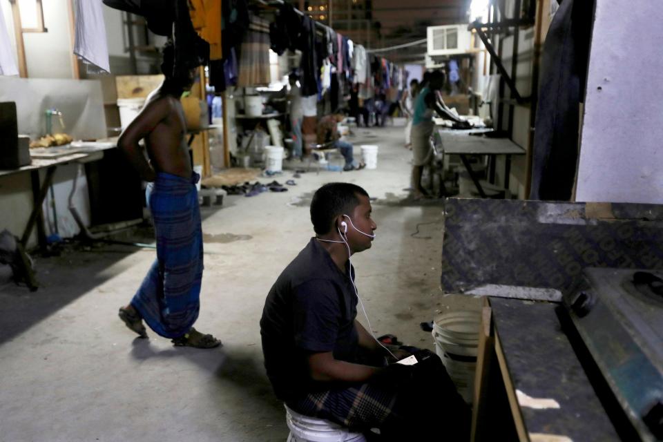 A labourer uses headphones to talk on his mobile phone as the others prepare dinner at their accommodations in the old Musheireb district of Doha, Qatar, Sunday, April 28, 2019.