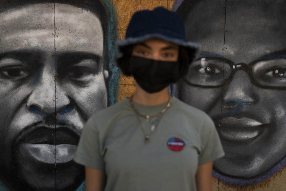 Saoirse McNamara, a 20-year-old model, pauses for photos with her "I Voted" sticker in front of a mural depicting George Floyd, left, and Elijah McClain Wednesday, Oct. 28, 2020, in Los Angeles. "I've actually taken a photo of this mural because I think it's really beautiful. It holds true to a lot of what's happened this year. It's really important for people to walk by this and to be reminded of what has happened this year and how there's definitely extreme changes that we have to make within our society," said McNamara who voted for Democratic presidential candidate former Vice President Joe Biden. (AP Photo/Jae C. Hong)