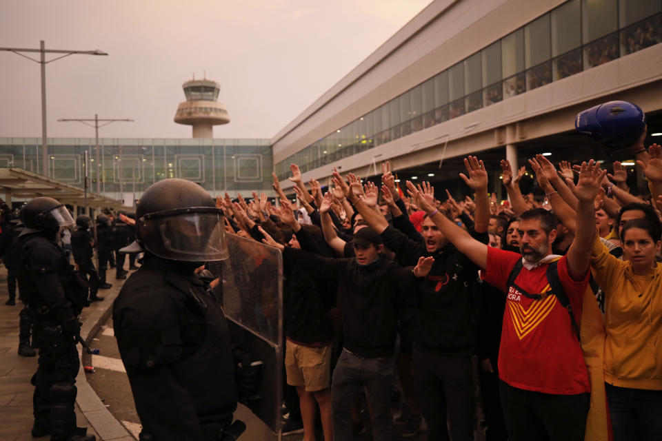 Protestors raise their arms in front of a line of riot policemen outside El Prat airport in Barcelona, Spain, Monday, Oct. 14, 2019. Riot police have charged at protesters outside Barcelona's airport after the Supreme Court sentenced 12 prominent Catalan separatists to lengthy prison terms for their roles in a 2017 push for the wealthy Spanish region's independence. (AP Photo/Emilio Morenatti)