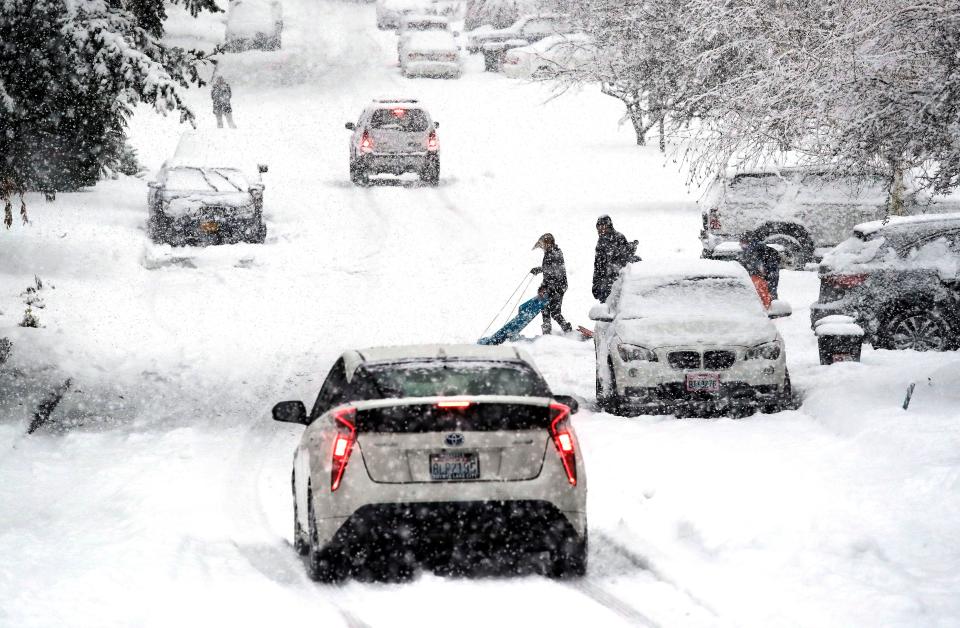 A sledder moves aside as traffic heads downhill in heavy snow falling Monday, Feb. 11, 2019, in Seattle.