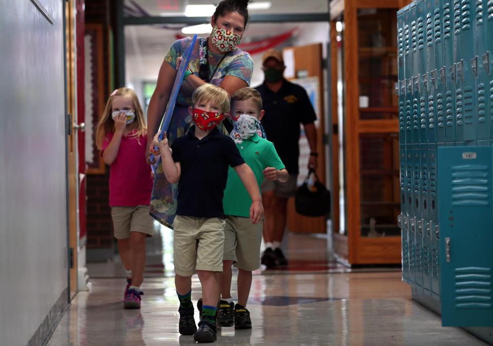 Kindergarten teacher Holly Rupprecht carries plexiglass panels to her room with help from Maelene Wright, left, her brother Hank Wright, and Rupprecht's son Theo at Zion Lutheran School in Bethalto, Ill. on Monday, July 20, 2020. The teacher designed her own table dividers with construction help from her father. (Robert Cohen/St. Louis Post-Dispatch via AP)