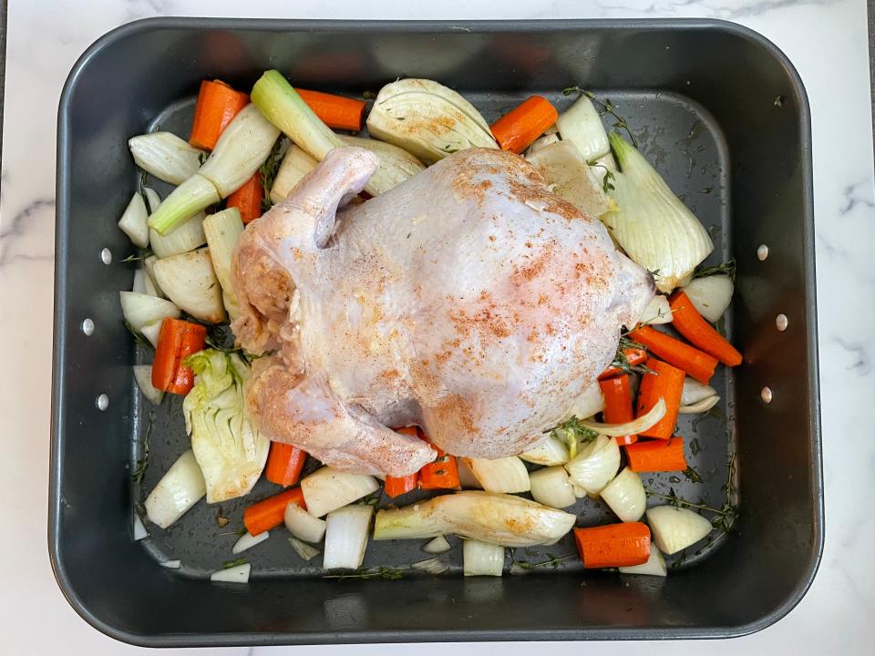 washed and stuffed chicken on top of cut vegetables in a roasting pan