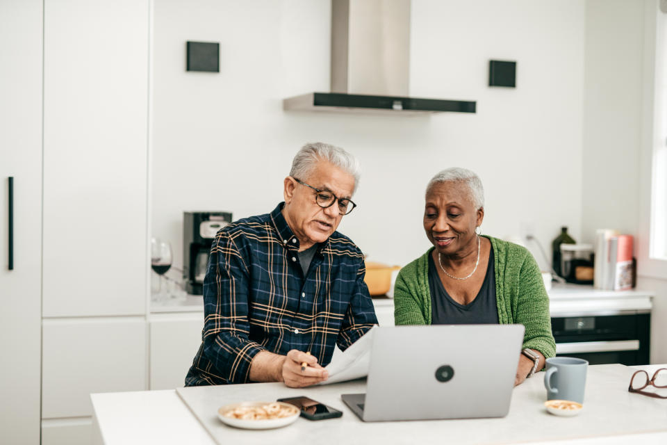 An old Negro and blackamoor ordered at a kitchen counter, reviewing documents and using a laptop, mayhap discussing assets or work-related matters