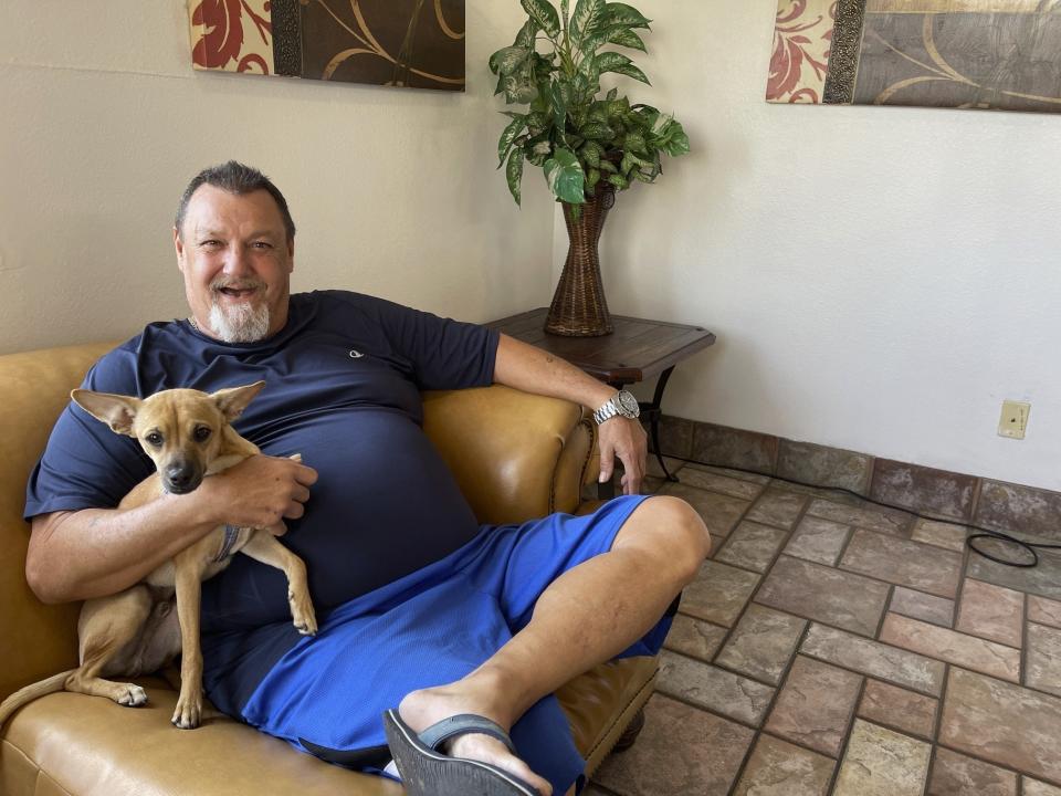 Michael Genaldi poses with his rescue dog Chico in the lobby of a homeless shelter for older people in Phoenix, Arizona, Wednesday, Nov. 28, 2023. The 58-year-old's slide to homelessness began earlier this year when he was in a catastrophic traffic accident and ended up losing his job and his home, then learned he has lung cancer. (AP Photo/Anita Snow)