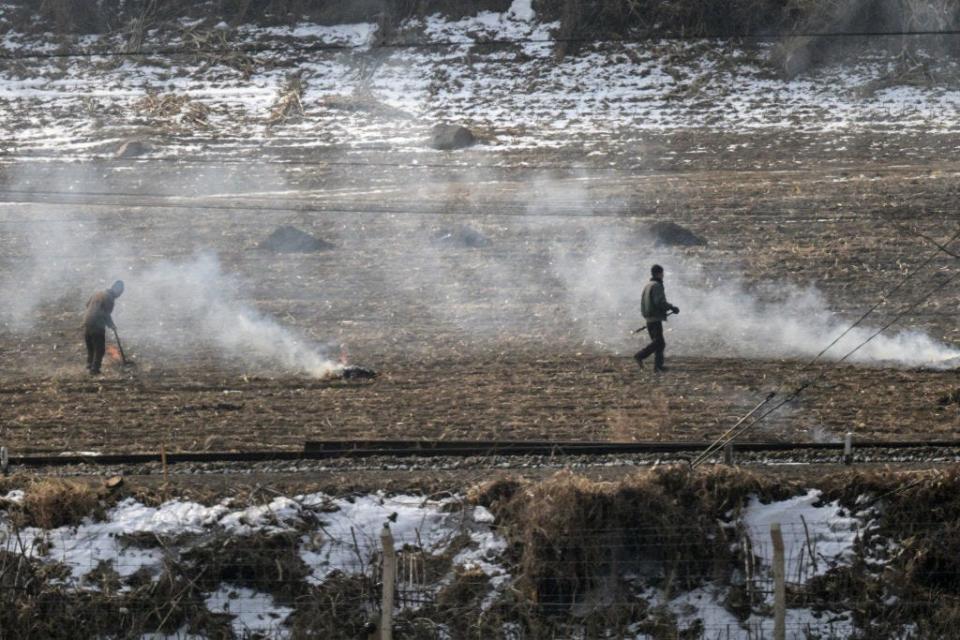 Two men working in brown field with snow around it.