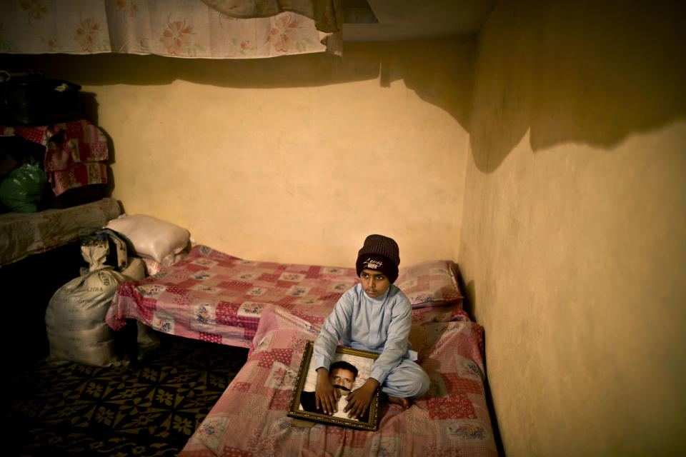 In this Tuesday, March 18, 2014 photo, Pakistani student, Danish Ali Hussein, 7, grandson of daily laborer, Talib Hussein, 54, who was one of eleven victims that was killed by suicide bombers in an attack on a court complex on March 3, 2014, sits on his late grandfather's bed and holds his photograph, at their home in a village near Islamabad, Pakistan. "I miss sleeping in my grandpa's arms," Danish said. (AP Photo/Muhammed Muheisen)
