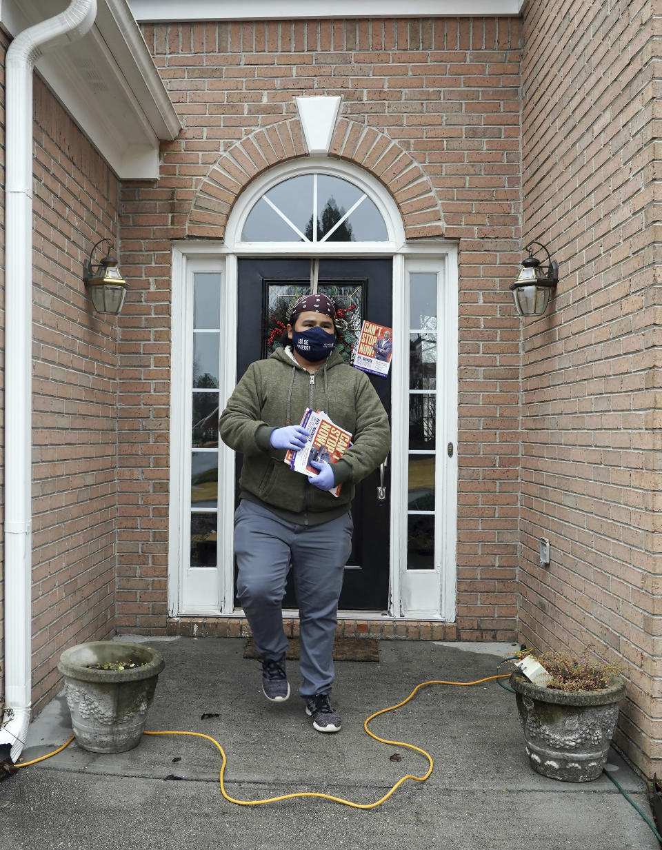 Graco Hernandez Valenzuela heads away after leaving a leaflet while canvassing a neighborhood for the Working Families Party regarding the U.S. Senate races, Wednesday, Dec. 16, 2020, in Lawrenceville, Ga. (AP Photo/Tami Chappell)