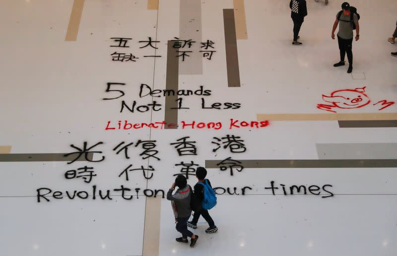 People walk past graffiti slogans written on the floor of a mall, in Hong Kong