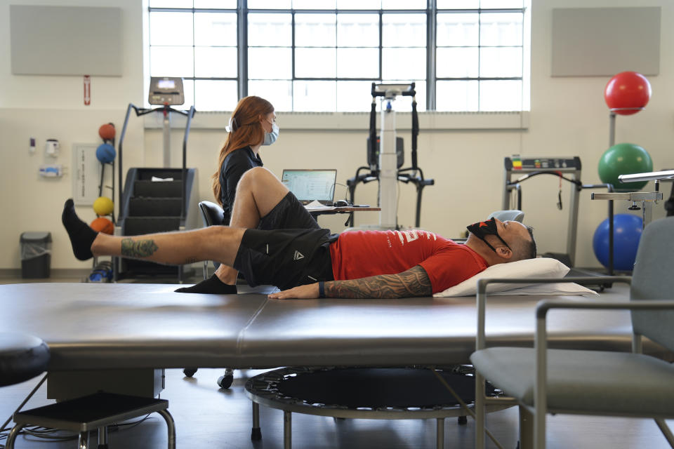 Patient Mike Camilleri works with physical therapist Beth Hughes in St. Louis, Mo., on March 1, 2023. Somehow, a mild case of COVID-19 set off a chain reaction that eventually left Camilleri with dangerous blood pressure spikes, a heartbeat that raced with slight exertion, and episodes of intense chest pain. (AP Photo/Angie Wang)