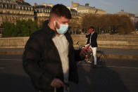 FILE - In this March 29, 2021 file photo, A man walks with a face mask to prevent the spread of the COVID-19 coronavirus, as a man takes a snapshot of the sunset, in Paris. France is lifting mandatory mask-wearing outdoors and will halt an eight-month nightly coronavirus curfew on June 20. (AP Photo/Thibault Camus, File)
