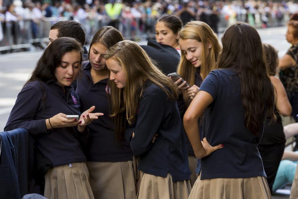 A group of Catholic school girls look at their phones as they wait on the route that Pope Francis will take later in the day near St. Patrick’s Cathedral in New York September 24, 2015.  Pope Francis concludes his visit to Washington, DC and continues onto New York later on Thurday. REUTERS/Lucas Jackson  - GF10000219612