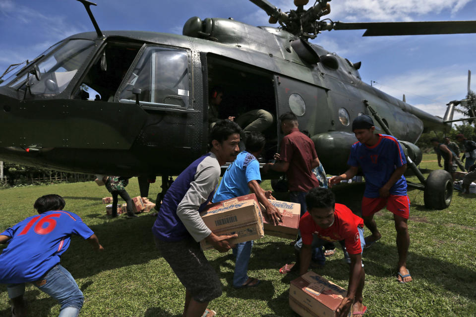 In this Oct. 7, 2018, file photo, earthquake survivors carry relief goods delivered by an Indonesian Army helicopter in Poroo, Central Sulawesi, Indonesia. (AP Photo/Dita Alangkara, File)