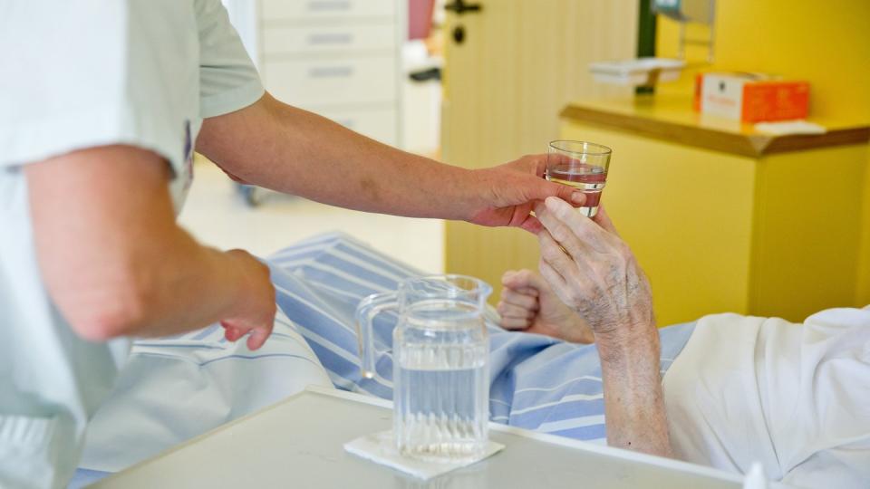 Eine Krankenpflegerin reicht einem Patienten in einem Klinikum ein Glas Wasser. Foto: Daniel Karmann