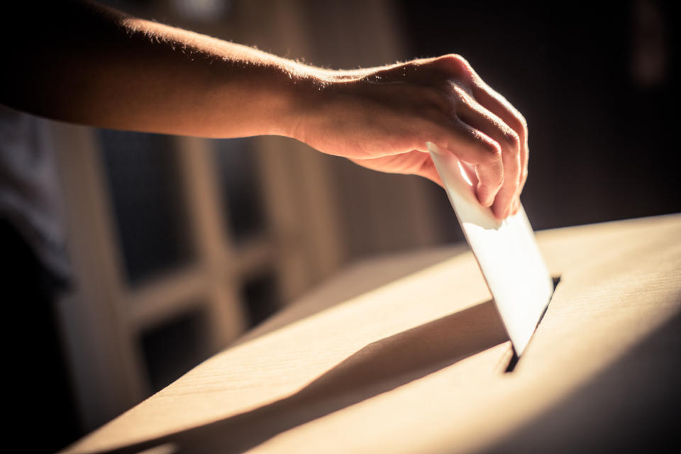 A person voting in a ballot box.