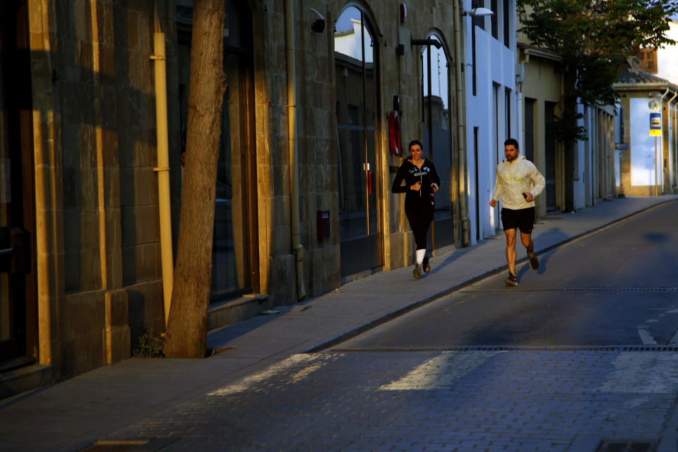 A couple jog in a street past closed shops, during the lockdown measures by government to prevent the spread of coronavirus pandemic in the medieval core in central capital Nicosia, Cyprus, on Wednesday, April 29, 2020. Cyprus' president Nicos Anastasiades announcements from May 4 the island starts to ease its lockdown restrictions from coronavirus pandemic. (AP Photo/Petros Karadjias)