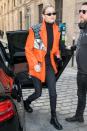 <p>in a bright orange patent leather oversized blazer over a tight black turtleneck, with black plaid pants, lace-up combat boots, and sunglasses.</p>