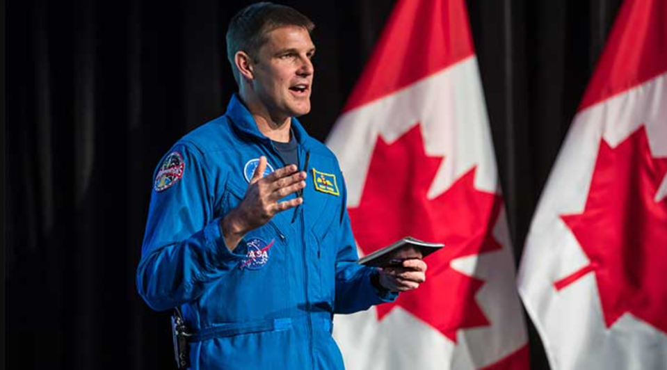 Artemis 2 moon astronaut Jeremy Hansen, of the Canadian Space Agency, speaks in front of two Canadian flags.