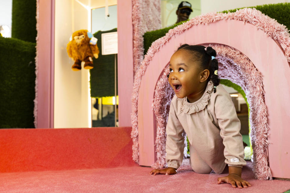 A baby crawling through a pink furry tunnel in the Young V&A museum