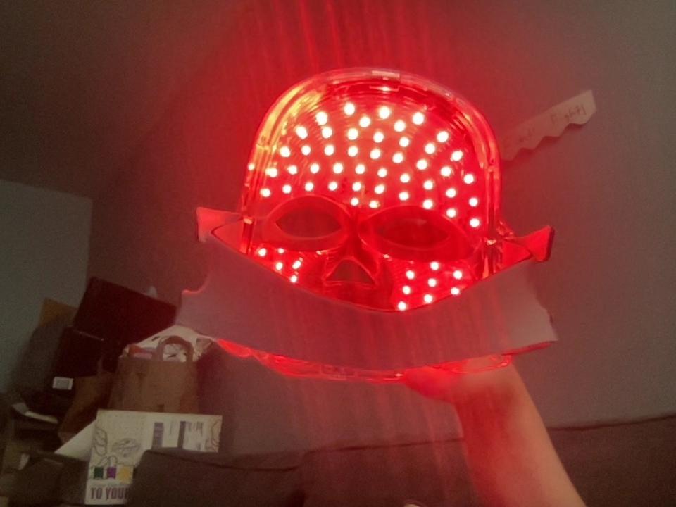 A backlit red LED mask against a dark living room background.