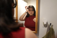 Daniella López White, of Hawaii, uses a mirror while adjusting her hair, Tuesday, May 14, 2024, at her apartment, in Boston. López White, who graduated from Emerson College in Boston this month and is on a tight budget, said TikTok influencers have helped her with tips on how to find affordable clothes at places like H&M and thrift shops. (AP Photo/Steven Senne)