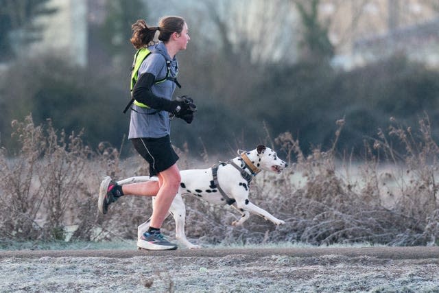 A woman and her dog run along the bank of the River Cam in Cambridge at sunrise