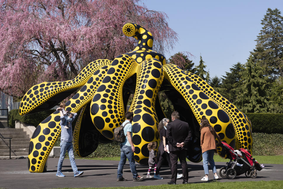 A family walks by one of Yayoi Kusama's pumpkin sculptures at the New York Botanical Garden, Thursday, April 8, 2021 in New York. The expansive exhibit has opened, and ticket sales have been brisk in a pandemic-weary city hungry for more outdoor cultural events. (AP Photo/Mark Lennihan)