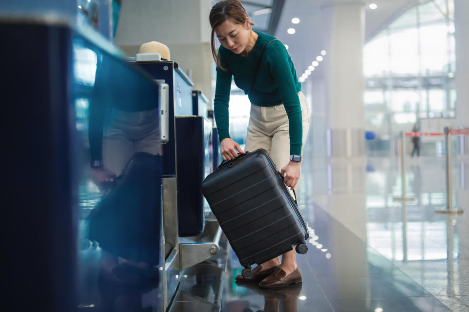 A person in a busy airport terminal is placing a suitcase onto a check-in counter