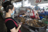 A customer wearing a face mask to protect from the new coronavirus orders food through plastic sheets at a market in Bangkok, Thailand, Thursday, April 23, 2020. A month-long state of emergency remain enforced in Thailand to allow its government to impose stricter measures to control the coronavirus that has infected hundreds of people in the Southeast Asian country. (AP Photo/Sakchai Lalit)