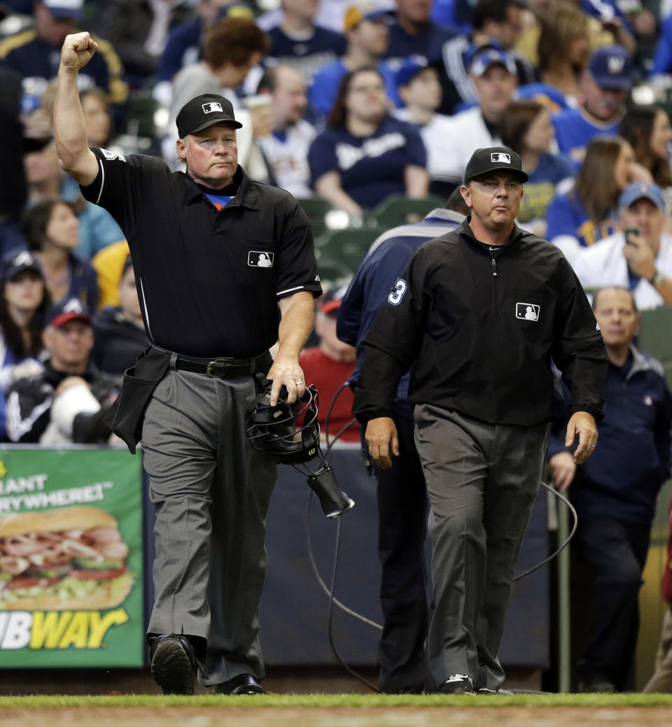 Umpire Ted Barrett, left, signals an out call after listening to the central replay booth in New York in the sixth inning of an opening day baseball game between the Atlanta Braves and Milwaukee Brewers, Monday, March 31, 2014, in Milwaukee. An umpire's call has been overturned for the first time under Major League Baseball's expanded replay system, with Brewers' Ryan Braun ruled out instead of safe. (AP Photo/Jeffrey Phelps)