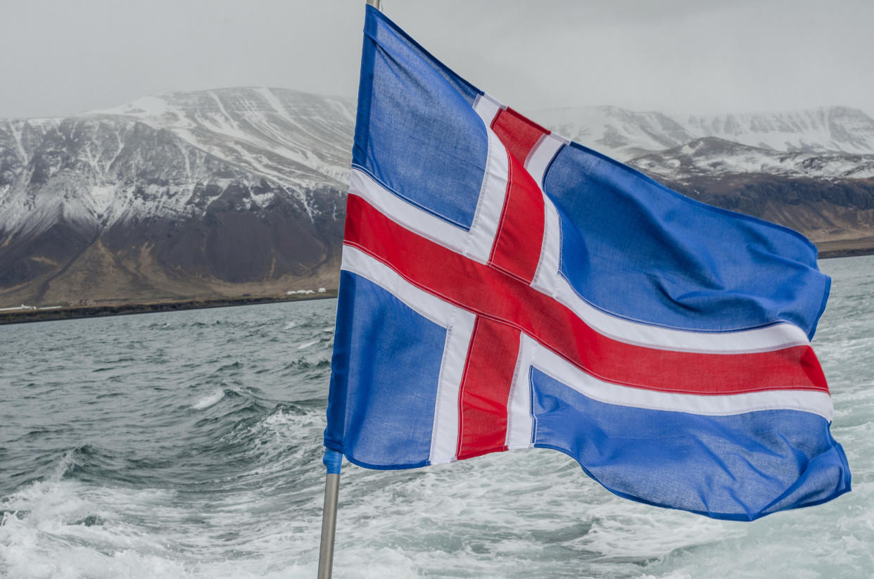 Cold day on Atlantic Ocean boat with misty mountains and Icelandic flag in foreground