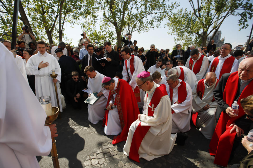 With Notre Dame cathedral, background right, religious officials pray during the Good Friday procession, Friday, April 19, 2019 in Paris. Top French art conservation officials say the works inside Notre Dame suffered no major damage in the fire that devastated the cathedral, and the pieces have been removed from the building for their protection.(AP Photo/Francois Mori)