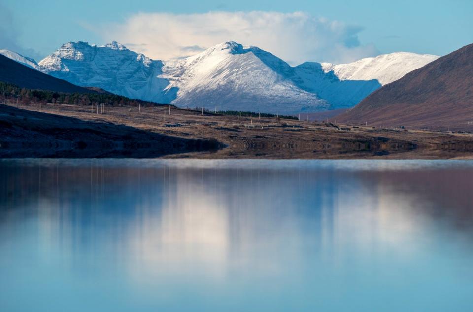 The snow-covered peak of Beinn Eighe and the mountains of Torridon reflected in Loch Glascarnoch near Ullapool, Wester Ross (PA)