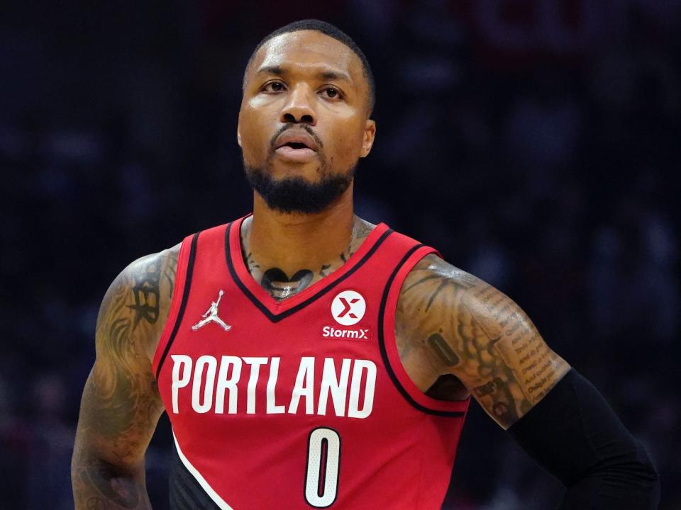 Damian Lillard stands with his hands on his hips and looks up.