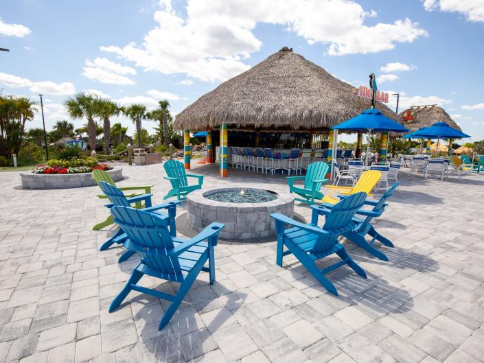 Lounge chairs surrounding a fire pit in front of a roof with a thatched pattern.