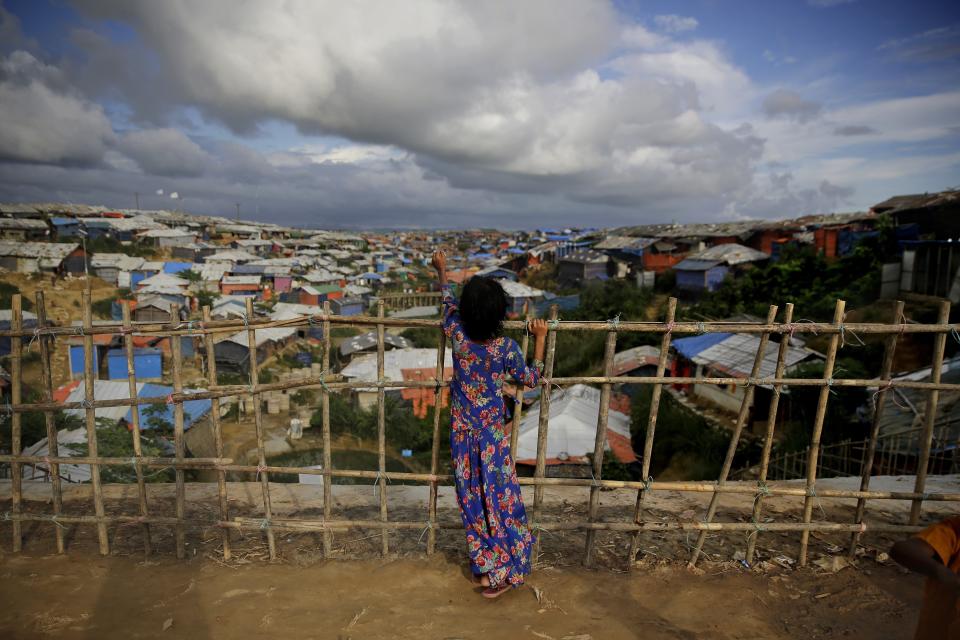 In this Aug. 26, 2018, photo, a Rohingya refugee girl stands by a fence at Kutupalong refugee camp, Bangladesh. More than half a million Rohingya children live in the congested camps. They rely on 1,200 learning centers set up by aid organizations that can’t accommodate everyone and only offer classes up to a 5th-grade level. (AP Photo/Altaf Qadri)