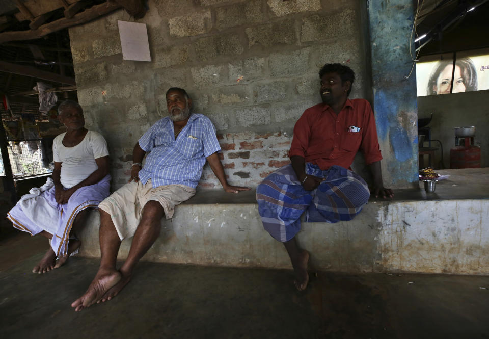 Villagers spend time next to a banner featuring U.S. Vice President-elect Kamala Harris, background right, in Thulasendrapuram, the hometown of Harris' maternal grandfather, south of Chennai, Tamil Nadu state, India, Wednesday, Jan. 20, 2021. A tiny village in a remote part of South India is gearing up for celebrations ahead of Kamala Harris' inauguration as the first female vice president of the United States. (AP Photo/Aijaz Rahi)