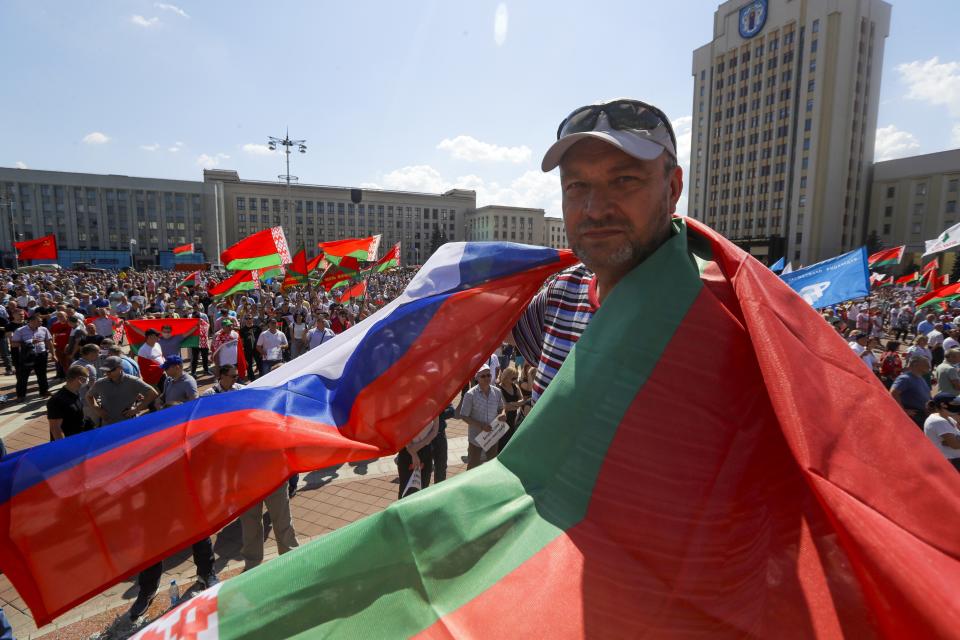 A man covers himself with Belarusian State and Russian national flags as supporters of Belarusian President Alexander Lukashenko gather at Independent Square of Minsk, Belarus, Sunday, Aug. 16, 2020. Thousands of people have gathered in a square near Belarus' main government building for a rally to support President Alexander Lukashenko, while opposition supporters whose protests have convulsed the country for a week aim to hold a major march in the capital. (AP Photo/Sergei Grits)