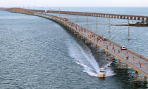 In this photo provided by the Florida Keys News Bureau, a boat cruises along the Seven Mile Bridge as a portion of 1,500 entrants compete in the annual Seven Mile Bridge Run Saturday, April 1, 2023, near Marathon, Fla. Joanna Stephens, 28, of Atlanta won the overall women's title and Vaclav Bursa, 15, of Big Pine Key, Fla., won the overall men's division. (Andy Newman/Florida Keys News Bureau via AP)