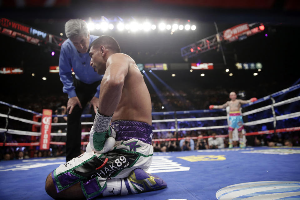 England's Amir Khan, left, kneels after receiving a low blow from Luis Collazo, right, in their silver welterweight title boxing fight Saturday, May 3, 2014, in Las Vegas. Referee Vic Drakulich looks on. Khan went on to win by unanimous decision. (AP Photo/Isaac Brekken)