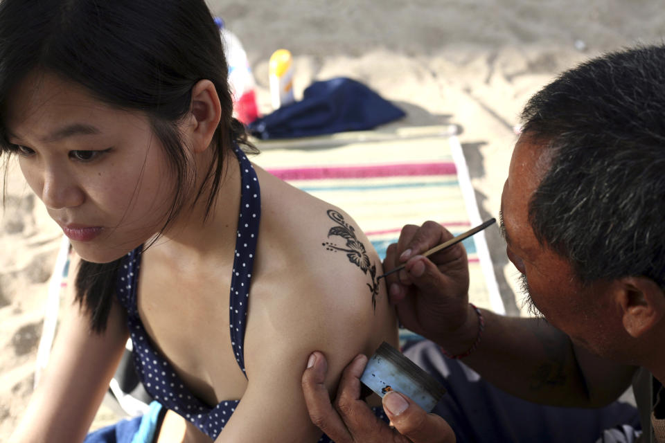 This Aug. 25, 2012 photo shows a Chinese tourist getting a temporary tattoo on Kuta beach, Bali, Indonesia. It can be hard to find Bali's serenity and beauty amid the villas with infinity pools and ads for Italian restaurants. But the rapidly developing island's simple pleasures still exist, in deserted beaches, simple meals of fried rice and coconut juice, and scenes of rural life. (AP Photo/Firdia Lisnawati)