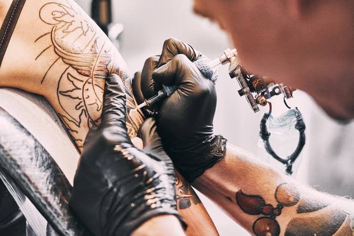 Close-up of a tattoo artist's gloved hands inking a sun and moon design on a person's upper arm