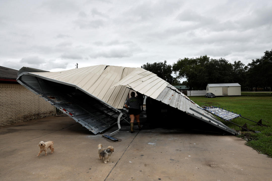 People beneath a knocked-down metal structure survey the damage.