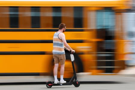 A scooter rider zooms past a parked school bus as he rides along the beach in San Diego , California