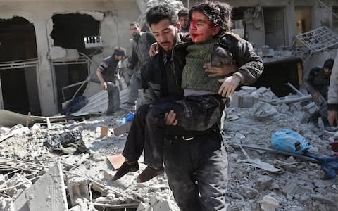 Syrians rescue a child following a reported regime air strike in the rebel-held town of Hamouria, in Eastern Ghouta  - Credit: ABDULMONAM EASSA/AFP/Getty Images